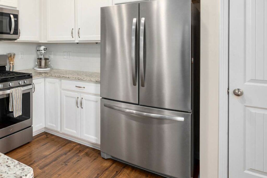 A modern kitchen featuring a white cabinet setup with a stainless steel French door refrigerator