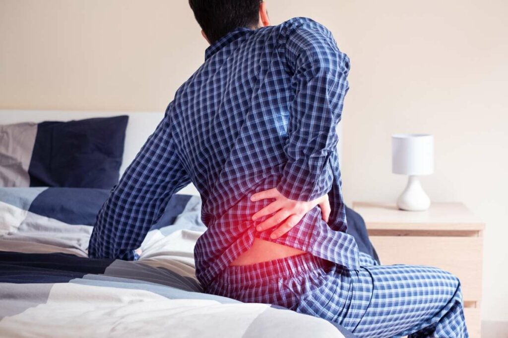 A man experiencing back pain while lying in bed due to the discomfort caused by the mattress