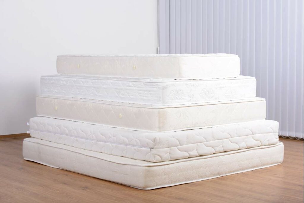 A stack of four mattresses on a hardwood floor, with a layer of old mattress underneath.