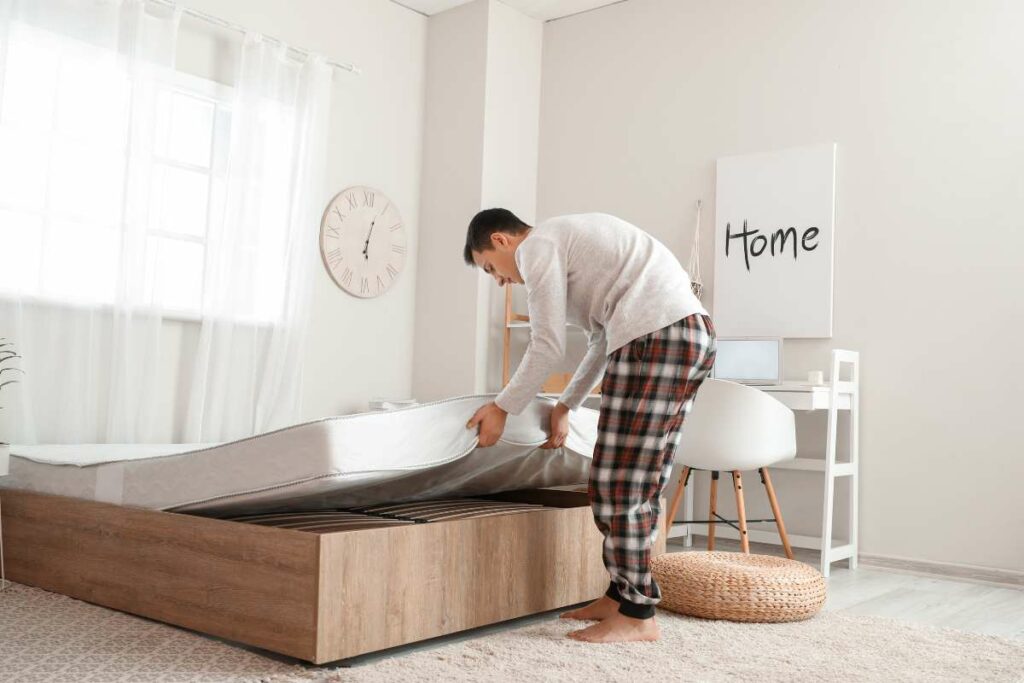 A man is placing a light weight mattress on a wooden bed frame.