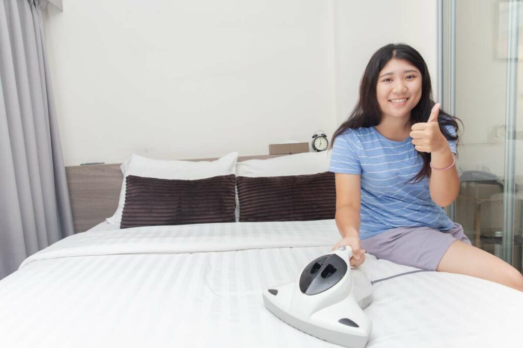 A woman seated on a bed, operating a vacuum cleaner to ensure the cleanliness and hygiene of the mattress.