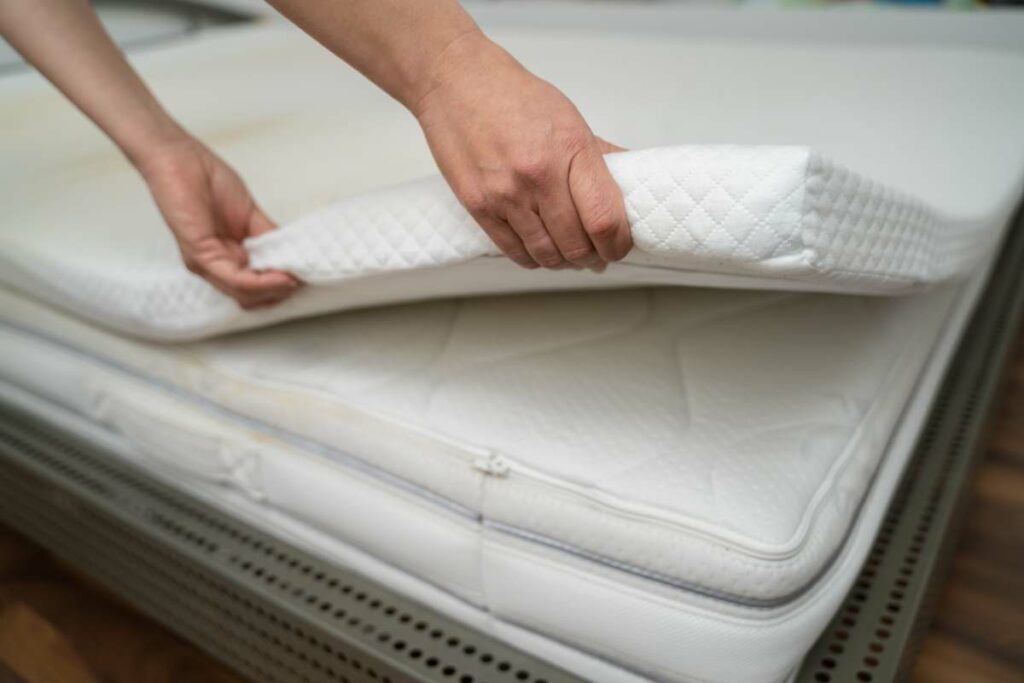 A person is placing a thick mattress on top of a bed.