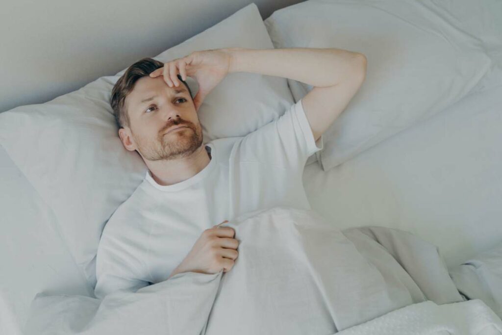A man laying in bed having an unrestful sleep due to a bad mattress with his head resting on his hand.