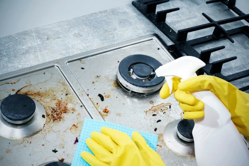 Person in yellow gloves cleaning gas stove top with cloth and spray