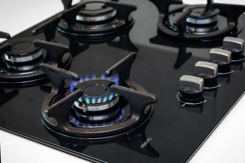 A sleek gas stove top featuring four burners, exuding modern elegance with its black color and glass top design.