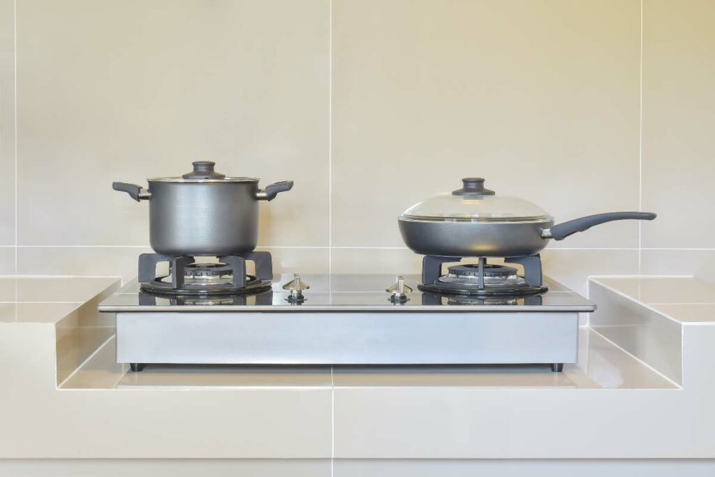 A stainless steel pots and pans placed on 2 stainless steel burner gas stove.
